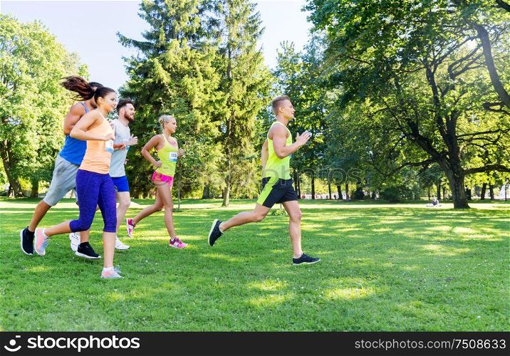 fitness, sport, race and healthy lifestyle concept - group of happy people or sportsmen running marathon with badge numbers at summer park. happy young sportsmen racing wit badge numbers