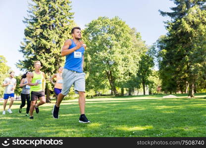 fitness, sport, race and healthy lifestyle concept - group of happy people or sportsmen running marathon with badge numbers at summer park. happy young sportsmen racing wit badge numbers