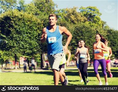 fitness, sport, race and healthy lifestyle concept - group of happy teenage friends or sportsmen running marathon with badge numbers outdoors