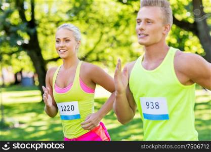 fitness, sport, race and healthy lifestyle concept - happy couple of sportsmen running marathon with badge numbers at summer park. happy couple of sportsmen racing wit badge numbers