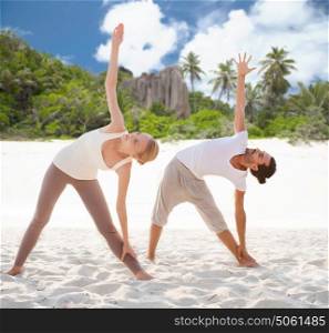 fitness, sport, recreation and people concept - couple making yoga left triangle pose over exotic tropical beach background. couple making yoga left triangle pose outdoors