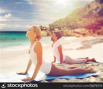 fitness, sport, recreation and people concept - couple making yoga upward facing dog pose on mat outdoors over exotic tropical beach background. couple making yoga upward facing dog pose outdoors
