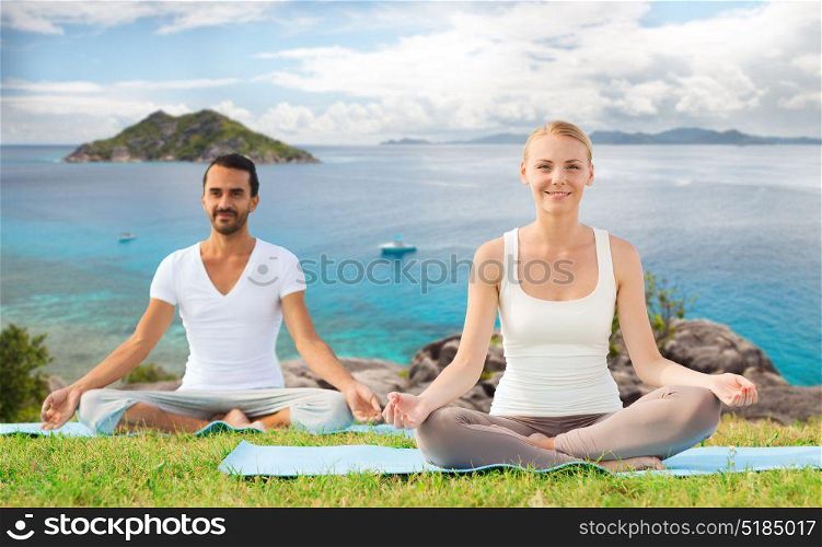 fitness, sport, recreation and people concept - happy couple making yoga exercises sitting on mats outdoors over ocean background. happy couple making yoga exercises outdoors