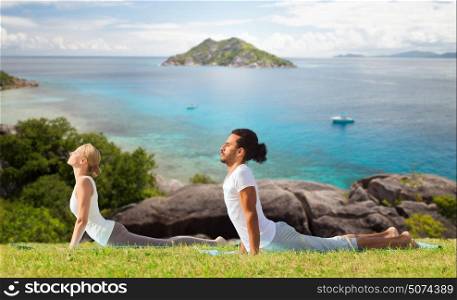 fitness, sport, relax and people concept - couple making yoga cobra pose over natural background. couple making yoga cobra pose outdoors