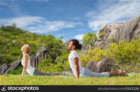 fitness, sport, relax and people concept - couple making yoga cobra pose over natural background. couple making yoga cobra pose outdoors