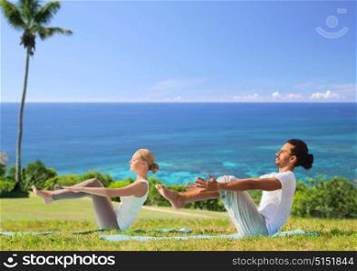 fitness, sport, relax and people concept - couple making yoga half-boat pose over exotic natural background with palm tree and ocean. couple making yoga half-boat pose outdoors