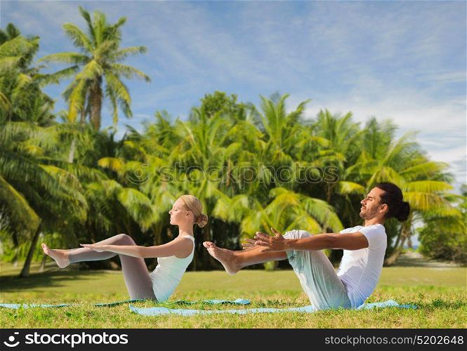 fitness, sport, relax and people concept - couple making yoga half-boat pose over exotic natural background with palm trees. couple making yoga half-boat pose outdoors