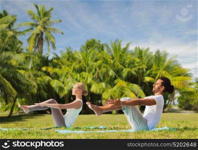 fitness, sport, relax and people concept - couple making yoga half-boat pose over exotic natural background with palm trees. couple making yoga half-boat pose outdoors