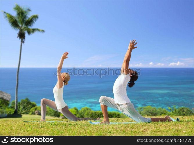 fitness, sport, relax and people concept - couple making yoga in low lunge pose over exotic natural background with palm tree and ocean. couple making yoga in low lunge pose outdoors
