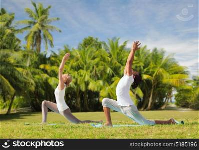 fitness, sport, relax and people concept - couple making yoga in low lunge pose over exotic natural background with palm trees. couple making yoga in low lunge pose outdoors