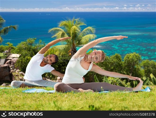 fitness, sport, relax and people concept - happy couple making yoga exercises sitting on mats outdoors over natural background. happy couple making yoga exercises outdoors