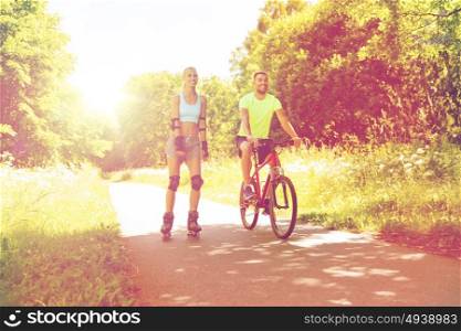fitness, sport, summer, people and healthy lifestyle concept - happy couple with rollerblades and bicycle riding outdoors at summer. happy couple with rollerblades and bicycle riding