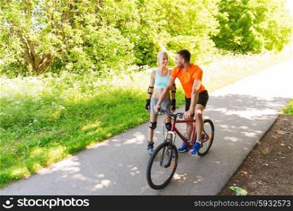fitness, sport, summer, people and healthy lifestyle concept - happy couple with rollerblades and bicycle riding and talking outdoors at summer