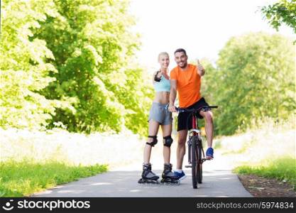 fitness, sport, summer, people and healthy lifestyle concept - happy couple with rollerblades and bicycle showing thumbs up outdoors at summer
