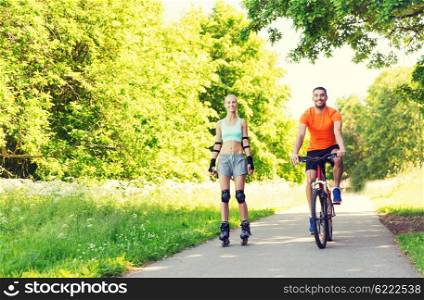 fitness, sport, summer, people and healthy lifestyle concept - happy couple with rollerskates and bicycle riding outdoors at summer