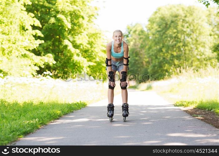 fitness, sport, summer, rollerblading and healthy lifestyle concept - happy young woman in rollerblades and protective gear riding outdoors