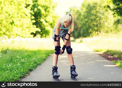fitness, sport, summer, rollerskating and healthy lifestyle concept - happy young woman in rollerskates and protective gear riding outdoors