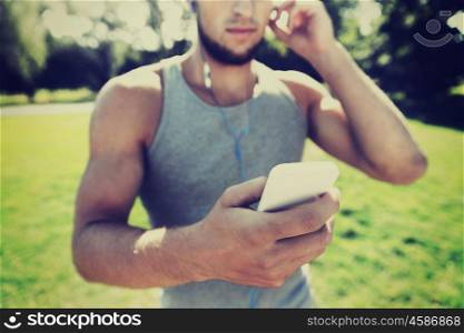 fitness, sport, technology and lifestyle concept - close up of young man with smartphone and earphones listening to music at summer park