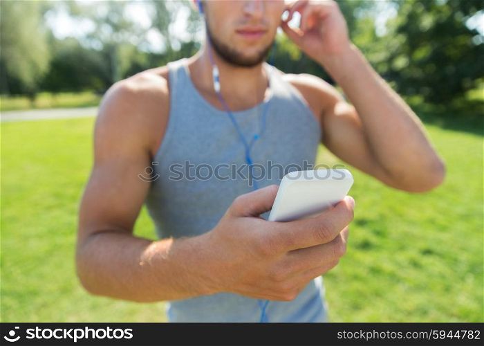 fitness, sport, technology and lifestyle concept - close up of young man with smartphone and earphones listening to music at summer park