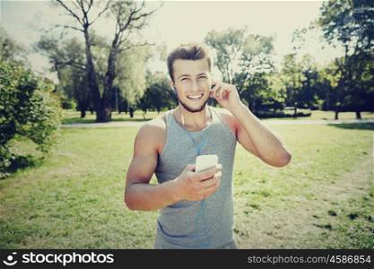 fitness, sport, technology and lifestyle concept - happy young man with smartphone and earphones listening to music at summer park