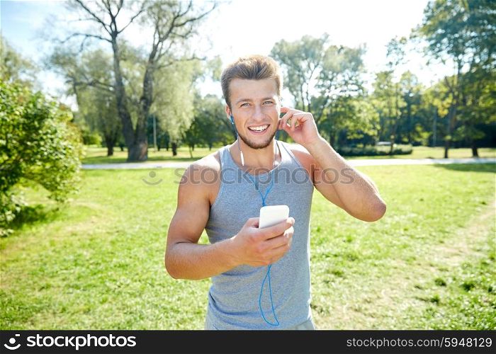 fitness, sport, technology and lifestyle concept - happy young man with smartphone and earphones listening to music at summer park