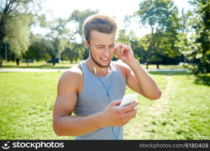 fitness, sport, technology and lifestyle concept - happy young man with smartphone and earphones listening to music at summer park