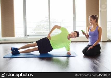 fitness, sport, technology and people concept - man and woman with smartphone doing side plank exercise on mat in gym