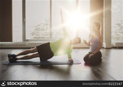 fitness, sport, technology and people concept - man and woman with smartphone doing side plank exercise on mat in gym