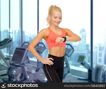 fitness, sport, technology, people and exercising concept - smiling woman looking at heart rate watch on hand over gym machines background