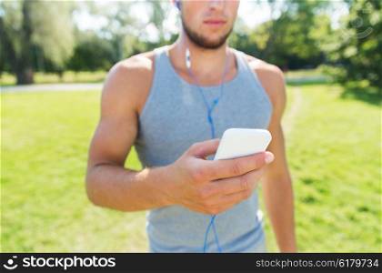 fitness, sport, technology, people and lifestyle concept - close up of young man with smartphone and earphones listening to music at summer park