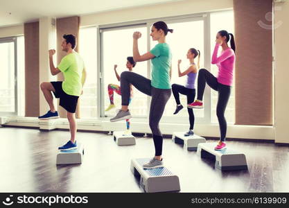 fitness, sport, training, aerobics and people concept - group of people working out with steppers in gym