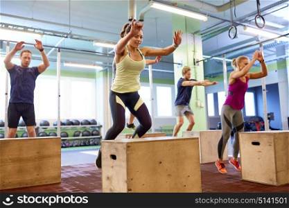 fitness, sport, training and exercising concept - group of people doing box jumps in gym. group of people doing box jumps exercise in gym
