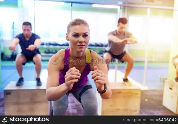 fitness, sport, training and exercising concept - group of people with heart-rate trackers doing box jumps in gym. group of people doing box jumps exercise in gym