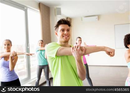 fitness, sport, training and exercising concept - group of smiling people stretching in gym