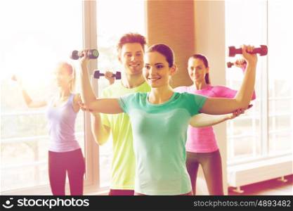 fitness, sport, training and exercising concept - group of smiling people working out with dumbbells flexing muscles in gym
