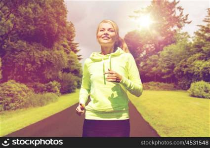 fitness, sport, training and exercising concept - happy smiling young woman jogging outdoors over road and natural background