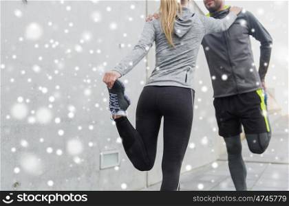 fitness, sport, training and healthy lifestyle concept - close up of couple stretching legs outdoors over snow