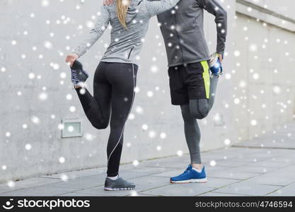 fitness, sport, training and healthy lifestyle concept - close up of couple stretching legs outdoors over snow