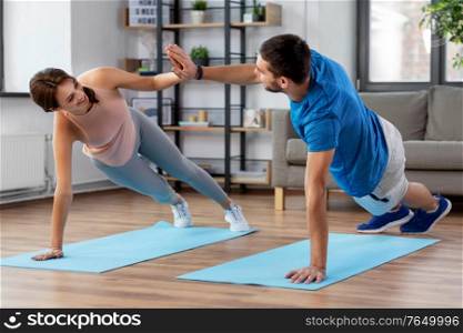 fitness, sport, training and healthy lifestyle concept - happy couple make high five in side plank at home. happy couple make high five in side plank at home