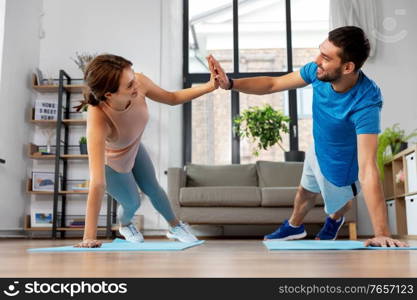 fitness, sport, training and healthy lifestyle concept - happy couple make high five in side plank at home. happy couple make high five in side plank at home