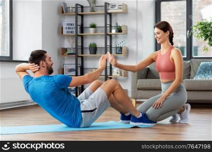 fitness, sport, training and healthy lifestyle concept - man with personal trainer doing sit ups at home. man with personal trainer doing sit ups at home
