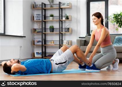 fitness, sport, training and healthy lifestyle concept - man with personal trainer doing sit ups at home. man with personal trainer doing sit ups at home