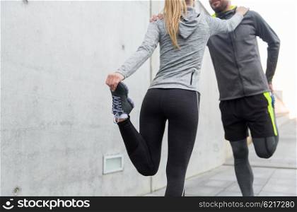 fitness, sport, training and lifestyle concept - close up of couple stretching legs outdoors