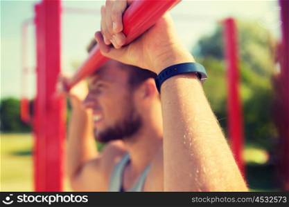 fitness, sport, training and lifestyle concept - close up of young man with heart-rate watch bracelet exercising on horizontal bar in summer park