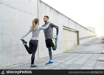 fitness, sport, training and lifestyle concept - couple of sportsmen stretching leg on city street