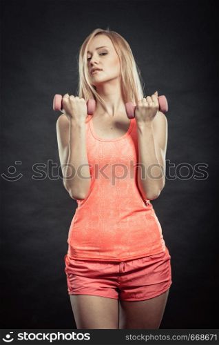 Fitness, sport, training and lifestyle concept. Fit woman with dumbbells flexing muscles in gym. Muscular blonde girl lifting light weights studio shot on black background