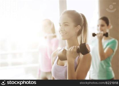 fitness, sport, training and lifestyle concept - group of happy women with dumbbells flexing muscles in gym