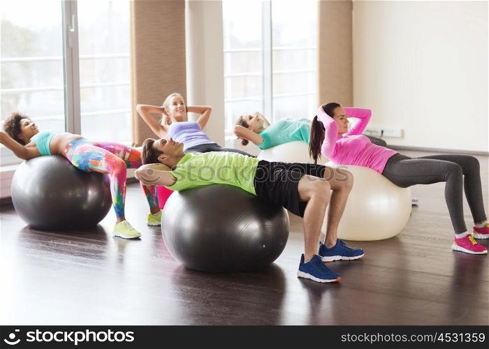 fitness, sport, training and lifestyle concept - group of people flexing abdominal muscles on fitball in gym