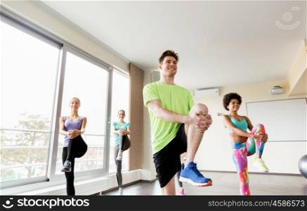 fitness, sport, training and lifestyle concept - group of smiling people with trainer exercising and stretching legs in gym