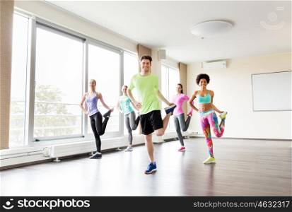 fitness, sport, training and lifestyle concept - group of smiling people with trainer exercising and stretching legs in gym